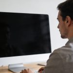 Homme assis a un bureau ecran noir