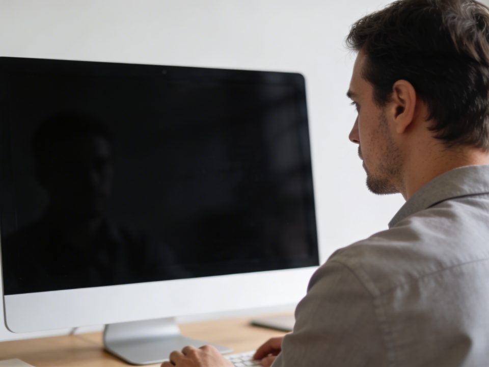 Homme assis a un bureau ecran noir