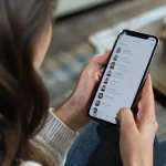 Main tenant un smartphone affichant une liste de contacts