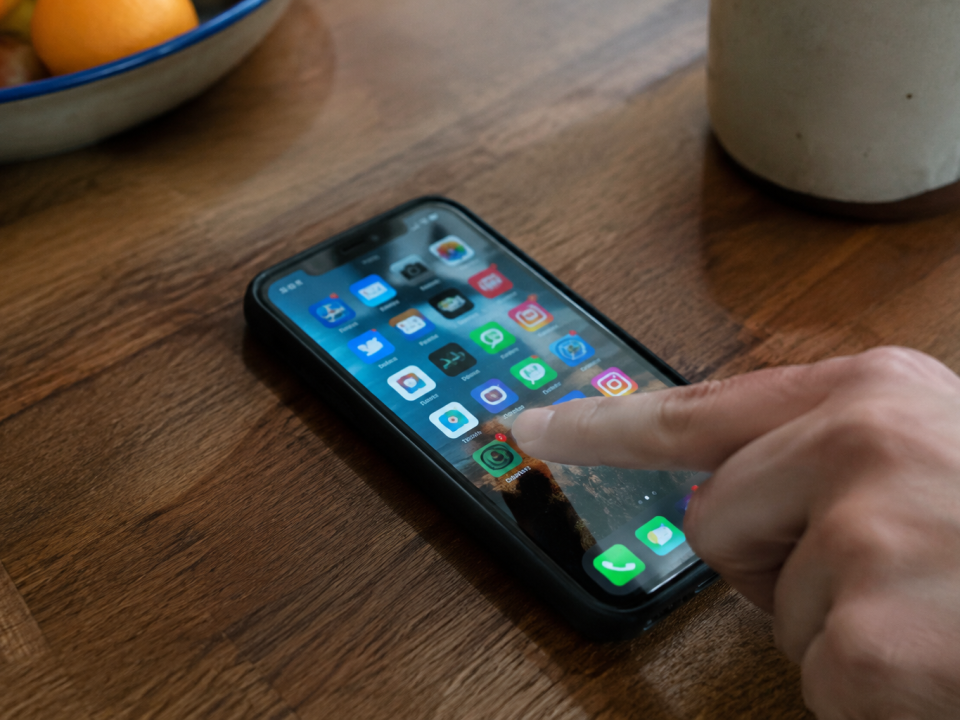 Smartphone pose sur table, pouce touchant une icone coloree